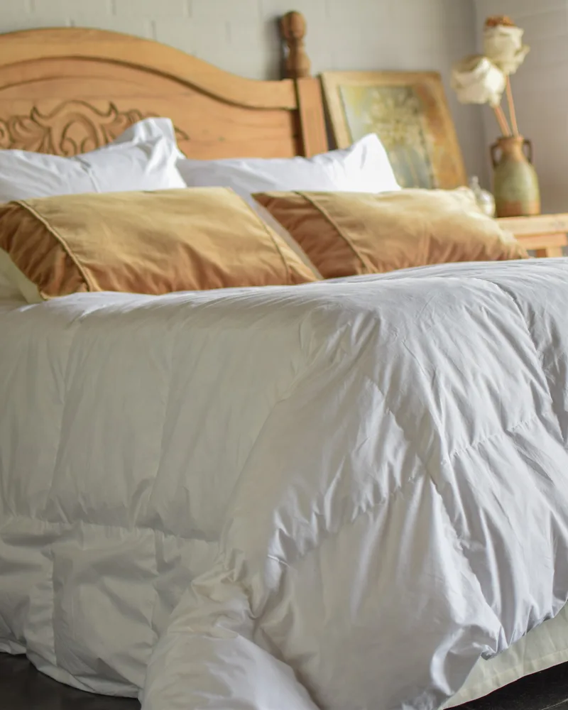 Cama tendida con un acolchado de pluma natural blanco y almohadones en tonos tierra