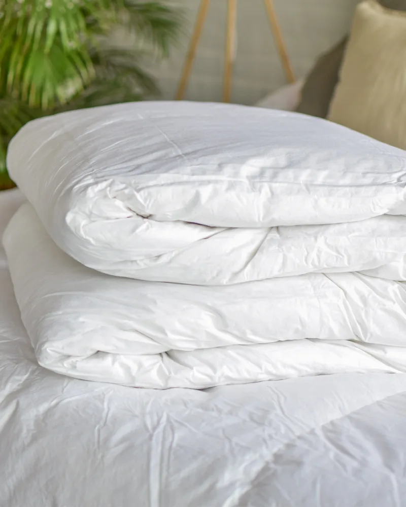 Acolchado de pluma sintética blanco doblado sobre la cama