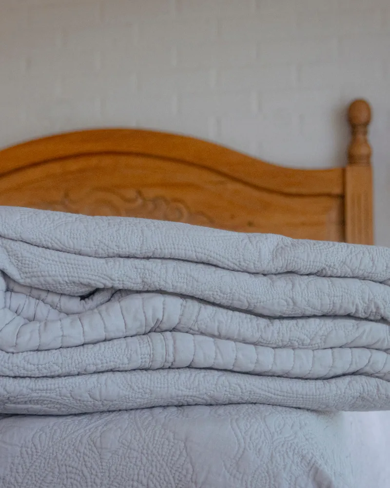 Cubrecama Chiara gris doblado sobre una cama con respaldo de madera