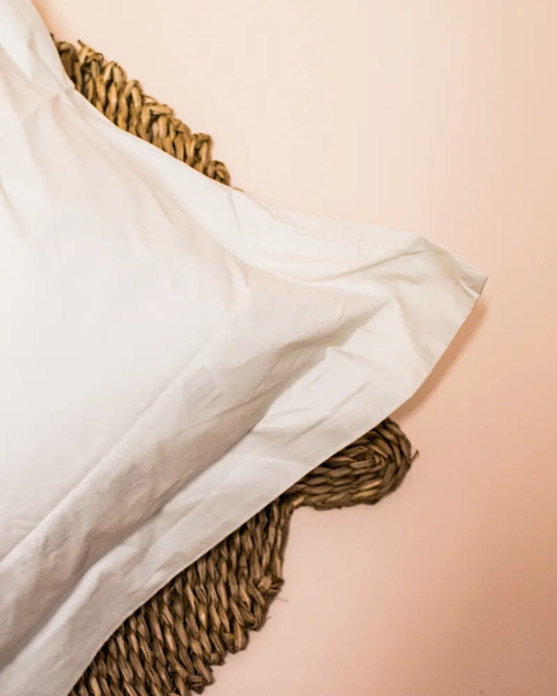 Almohada con funda blanca apoyada sobre un canasto de fibra